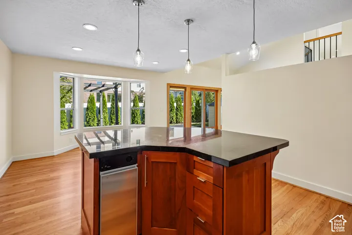 Kitchen island with dark countertop, integrated dishwasher, and rich wood cabinetry