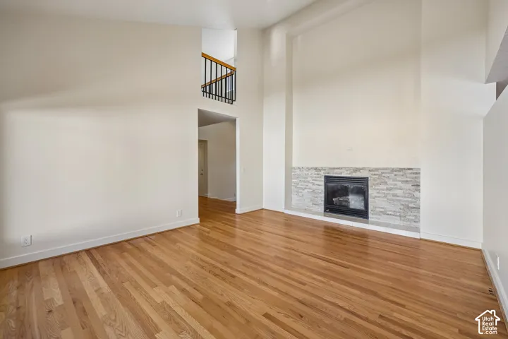 Hardwood flooring, fireplace with stacked stone surround, high ceilings, and an interior balcony with black metal railing