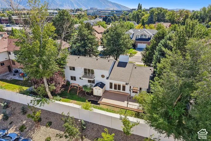 Expansive rear yard featuring a large wood-finish deck, mature trees, and a white privacy fence