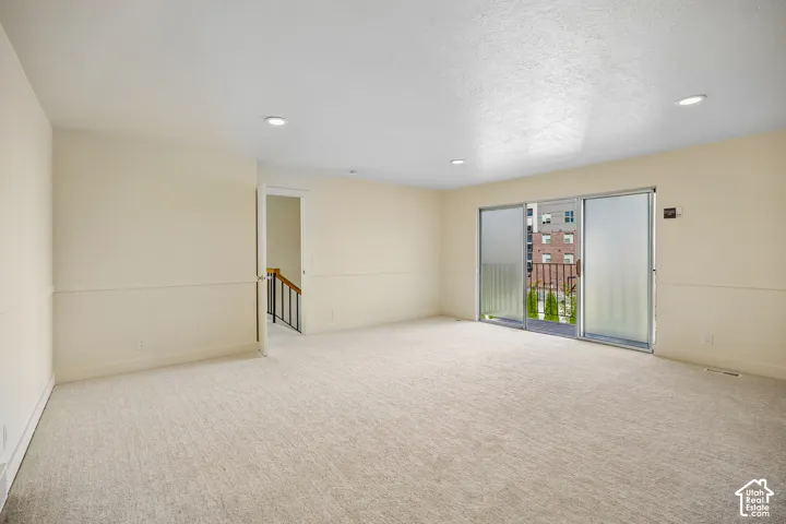 Expansive carpeted room with recessed lighting and a sliding glass door