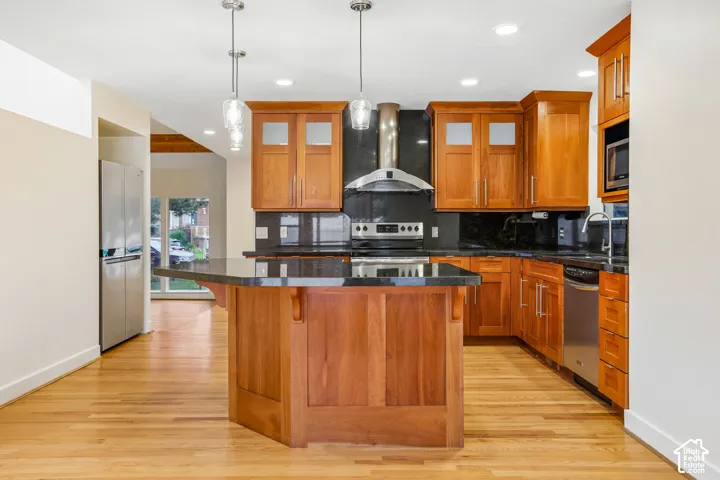 Kitchen featuring wood cabinetry, stainless steel appliances, dark countertops, and wood-finish flooring