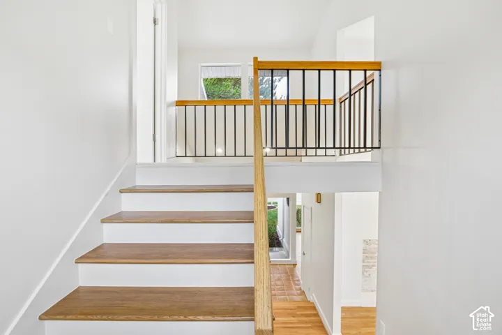 Wood-finish stairs with white risers and a light wood-finish handrail, complemented by a black metal balustrade