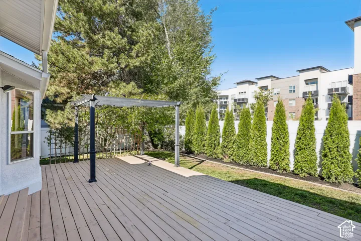 Expansive wood-finish deck with a pergola, bordered by a privacy fence and a row of evergreen trees