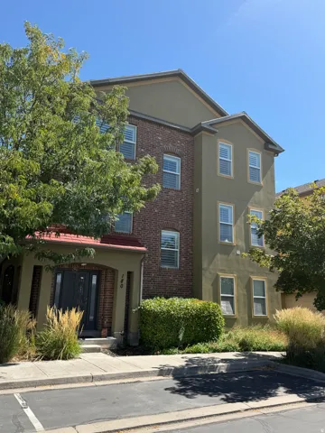 Multi-level exterior with brick and stucco finishes, covered entry, and mature landscaping