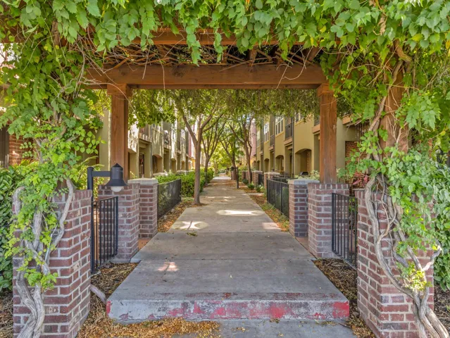 Vine-covered wooden arbor entrance with brick columns and wrought iron fencing