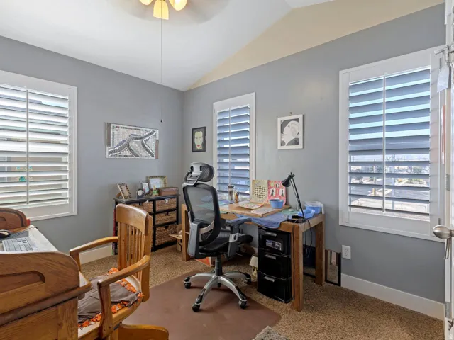 Vaulted ceiling with an attached ceiling fan, three windows with plantation shutters, and textured carpeting