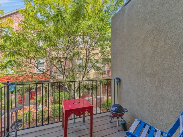 Balcony with wood-finish flooring, black wrought-iron railing, and a textured stucco exterior wall
