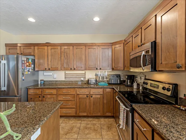 Kitchen featuring wood cabinetry, granite countertops, stainless steel refrigerator, stainless steel microwave, and tile flooring