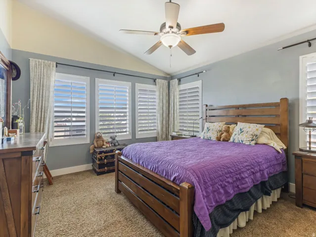 Vaulted ceiling with a ceiling fan, three windows with plantation shutters, and carpet flooring