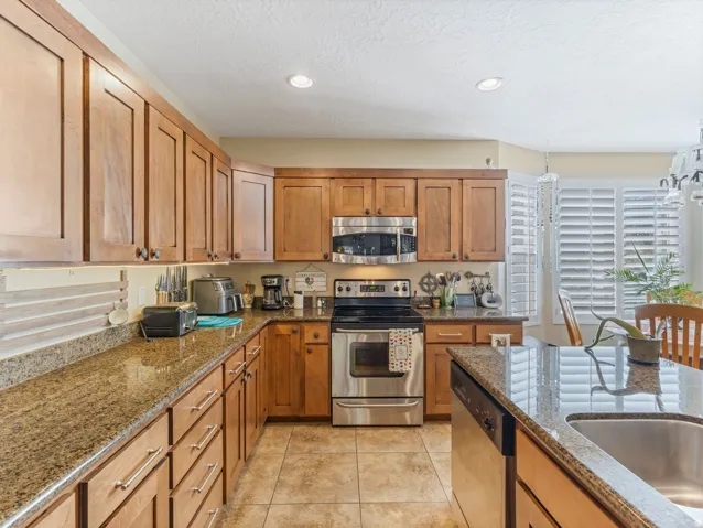 Kitchen featuring wood cabinetry, stainless steel appliances, granite countertops, an undermount sink, and recessed lighting