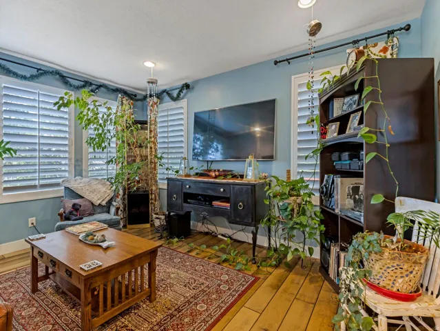 Wood-finish flooring, white plantation shutters, built-in media console, and recessed ceiling lighting