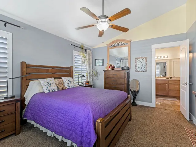 Room featuring a ceiling fan with integrated lighting, window shutters, and an attached bathroom with a dual vanity