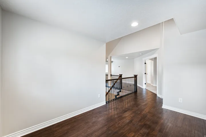 Wood-finish flooring, white walls, recessed ceiling lighting, open doorway, and dark wood newel posts with black metal balusters