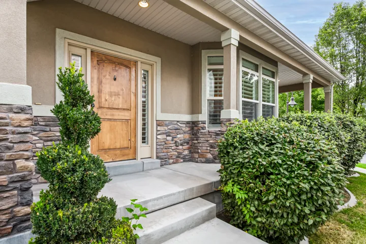 Front entry with stone veneer accents, natural wood door, concrete steps, and a covered porch