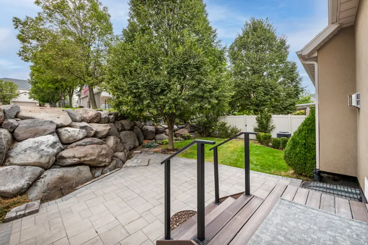 Paved patio area with a stone retaining wall and a sloped lawn