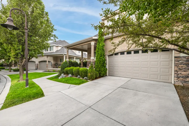 Exterior featuring a two-car garage, stacked stone accents, decorative landscaping, and a covered porch with columns
