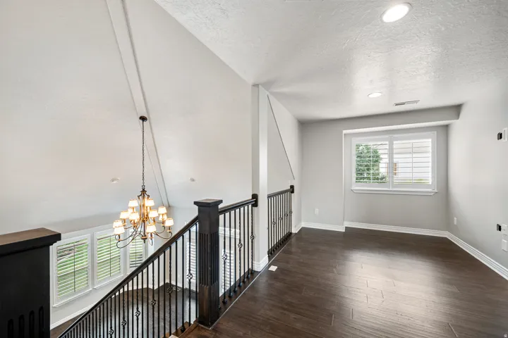 Vaulted ceilings, a decorative chandelier, and dark wood-finish flooring
