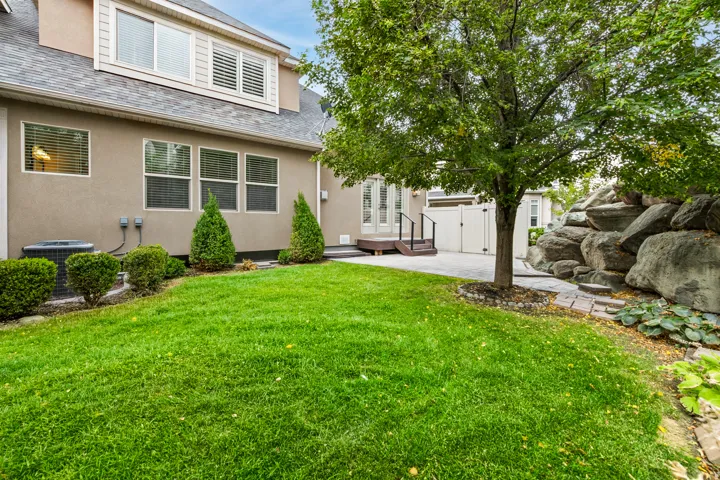 Expansive green lawn with a mature tree, leading to a paver patio and a rock garden feature