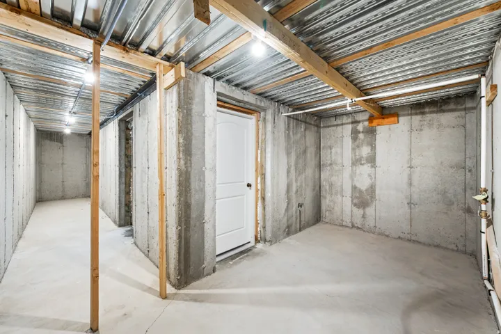 Unfinished basement with exposed concrete walls, exposed ceiling joists, and a white interior door