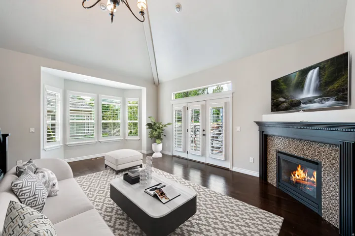 Varnished wood flooring, built-in fireplace with tile surround, vaulted ceiling, bay windows, and double French doors