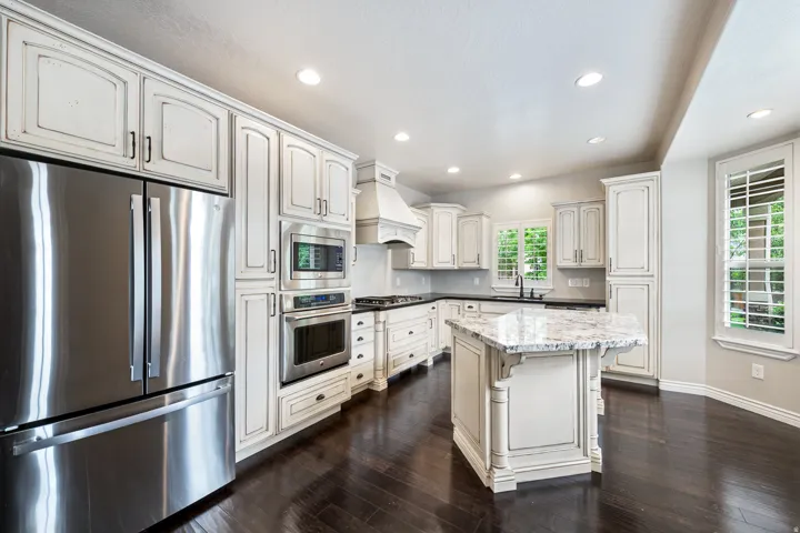 Gourmet kitchen with stainless steel appliances, white cabinetry, dark wood-finish flooring, recessed lighting, and a stone-topped island