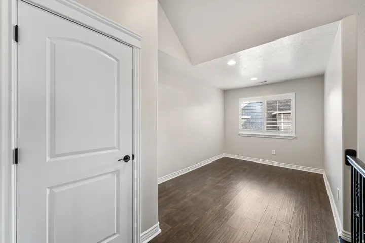 Wood-finish flooring, recessed lighting, window with horizontal blinds, interior paneled door with dark hardware, and sloped ceiling