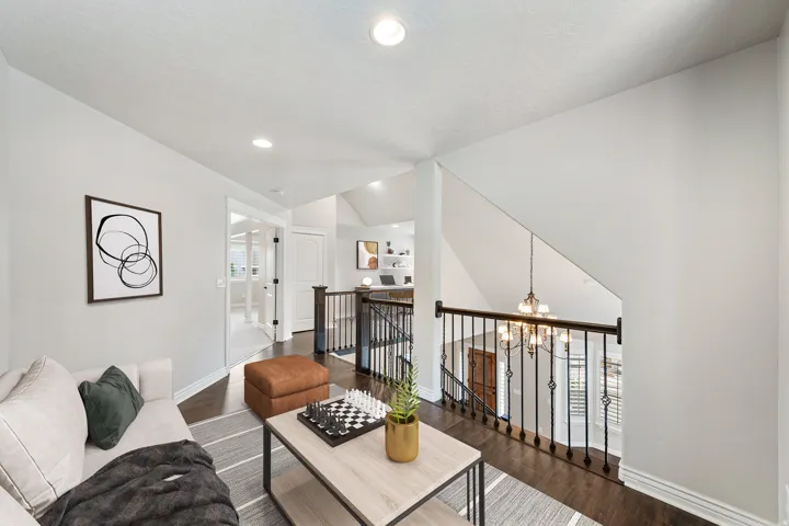 Recessed lighting illuminates this versatile loft space featuring rich wood-finish flooring and a decorative metal railing