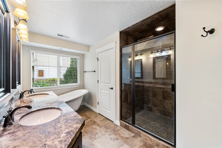 Dual vanity with integrated sinks and dark bronze fixtures, freestanding bathtub, and a glass-enclosed shower with tiled walls and a pebble floor
