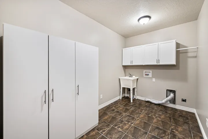 Utility room featuring built-in cabinetry, wall-mounted storage, a utility sink, and tile flooring