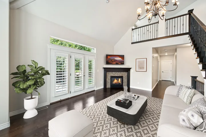 Living area with vaulted ceilings, dark wood-finish flooring, a tiled fireplace with mantel, and white plantation shutters on French doors