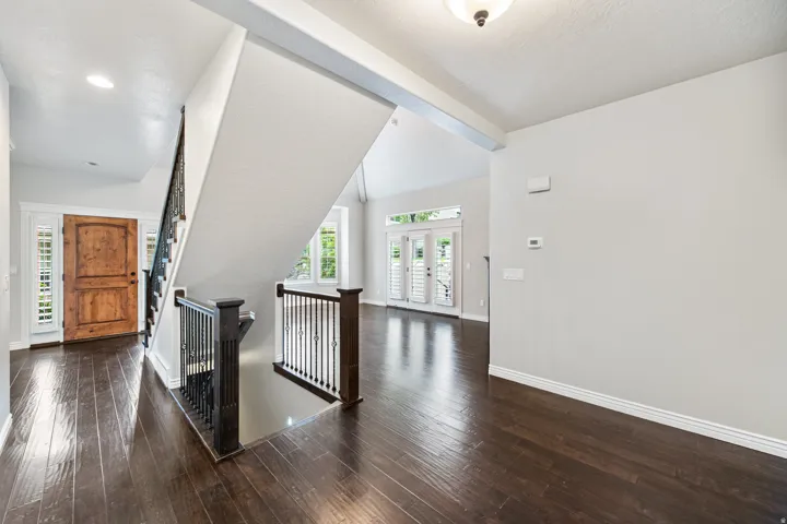 Hardwood flooring, wrought iron staircase with dark wood newel posts, vaulted ceiling, solid wood entry door with sidelights, and French doors with plantation shutters