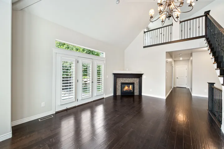 Vaulted ceiling with a decorative chandelier, dark wood-finish flooring, fireplace with a tile surround, and French doors with shutter blinds