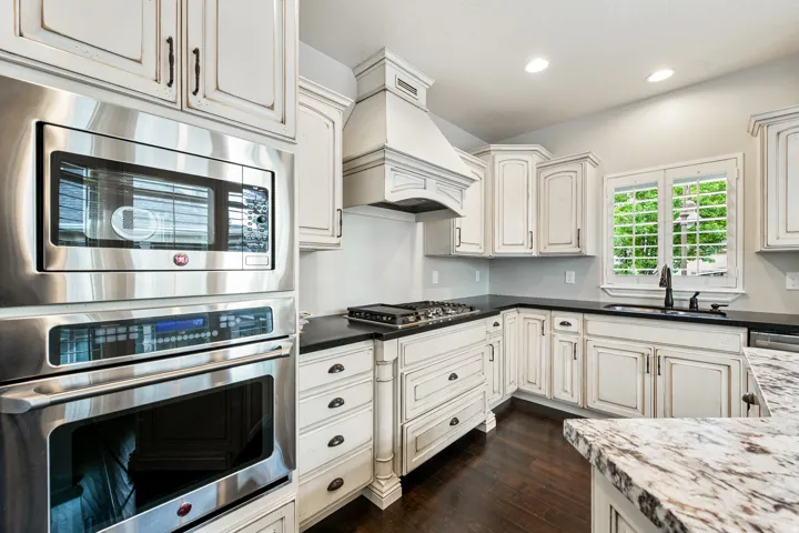 Stainless steel built-in microwave and oven, dark wood-finish flooring, white cabinetry with dark hardware, dark countertops, and a white granite-finish island countertop
