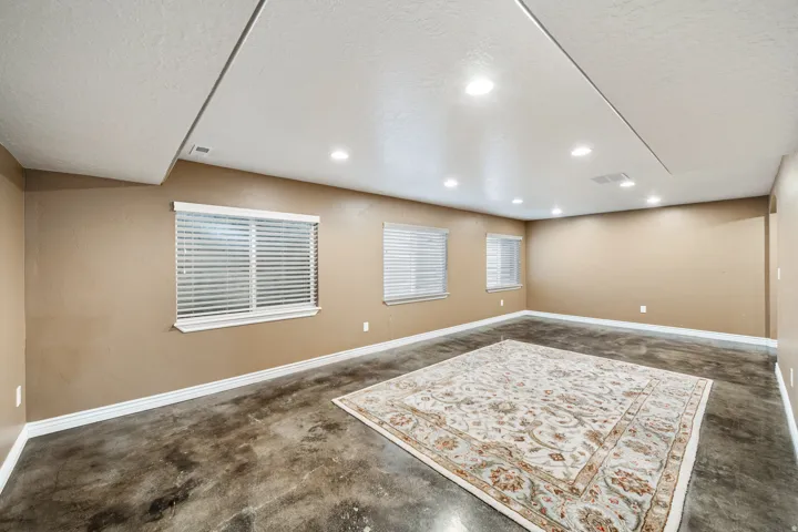 Recessed ceiling lighting, multiple windows with blinds, light-toned wall paint, and concrete flooring