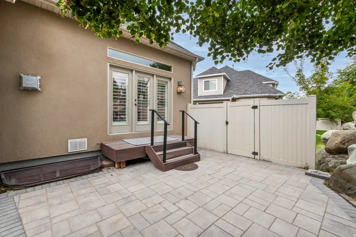 Stucco exterior with French doors, an elevated wood-finish deck with steps, a paved patio, and a privacy fence with gates