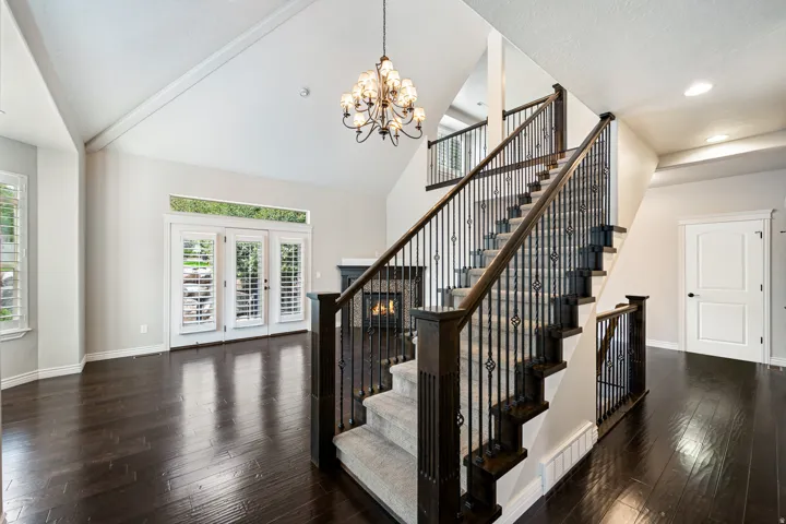 Vaulted ceiling, dark wood-finish flooring, fireplace with stone surround, wrought iron staircase, and French doors with transom window