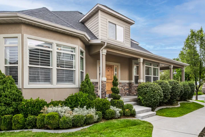 Stucco and stone exterior with a covered porch, established landscaping, and a concrete pathway