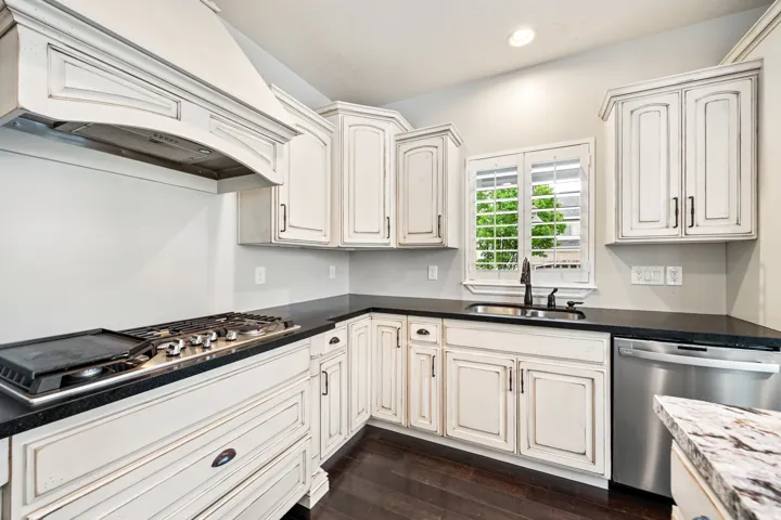Kitchen featuring distressed white cabinetry, black countertops, a stainless steel gas range with griddle, a built-in range hood, and a stainless steel dishwasher