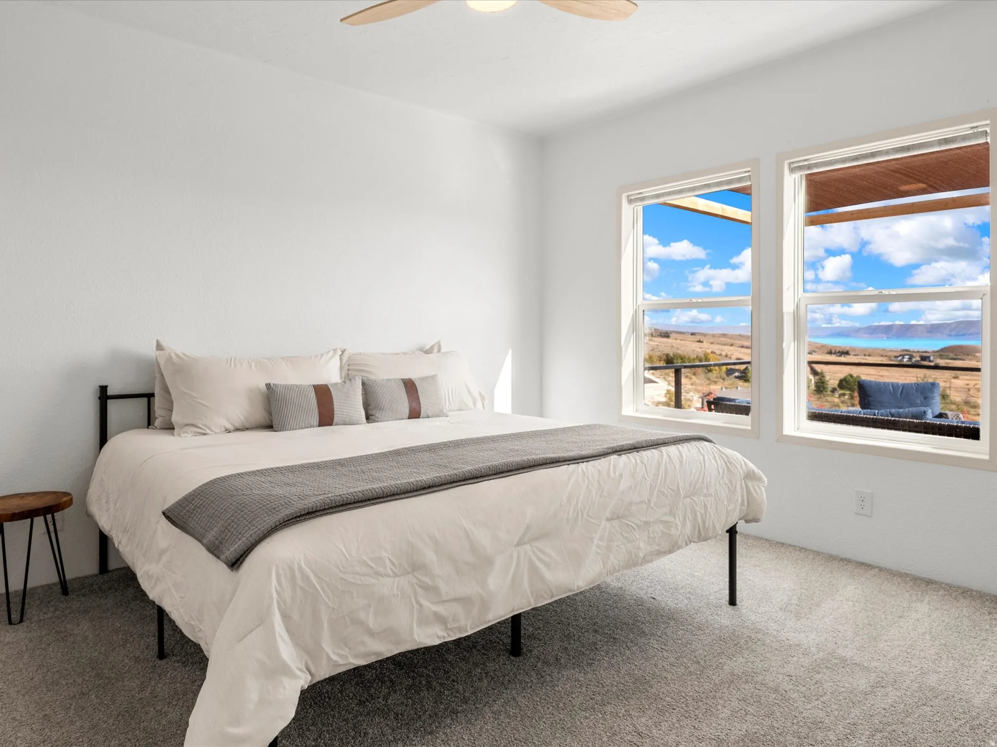 White walls, light-colored carpeting, two large windows, wood-finish ceiling fan with integrated lighting