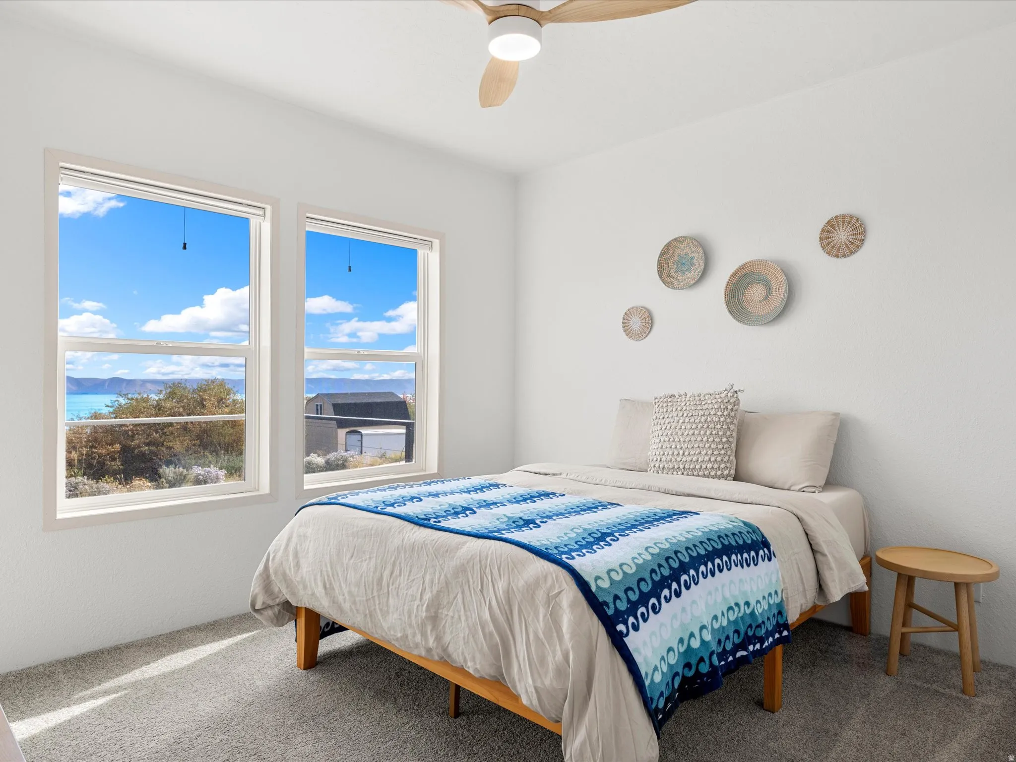 Dual windows, light wood-tone ceiling fan, and light gray carpeted flooring