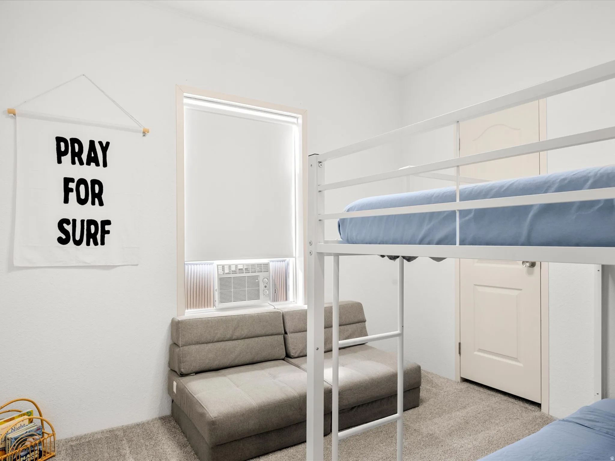White interior walls, a window with a roller shade, light-colored carpeting, a white interior door, and a window air conditioning unit