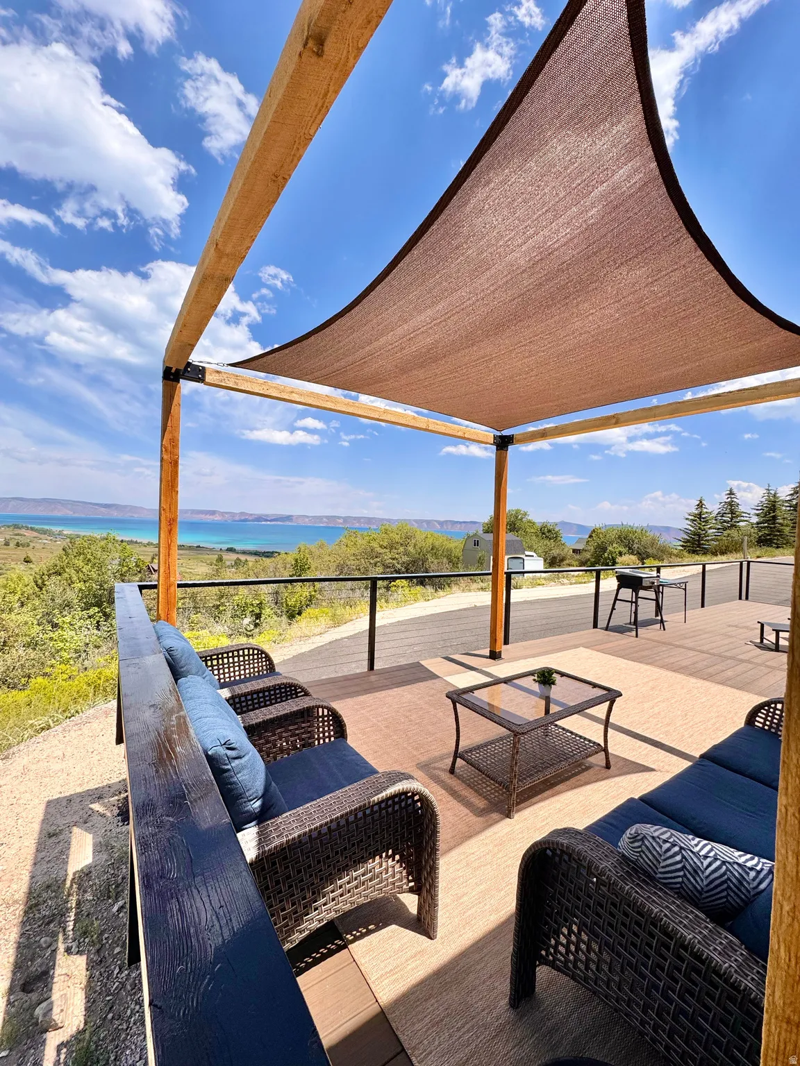 Expansive outdoor deck featuring a shade sail, wood pergola, and metal railing