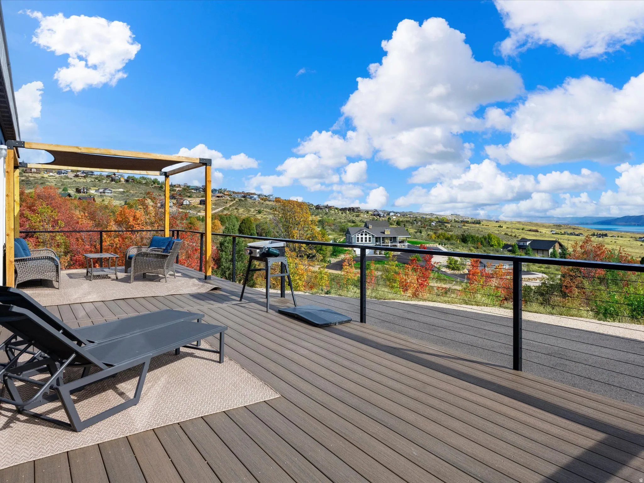 Expansive composite decking featuring a cable railing system, a wood pergola with a sunshade, and a broad landscape backdrop