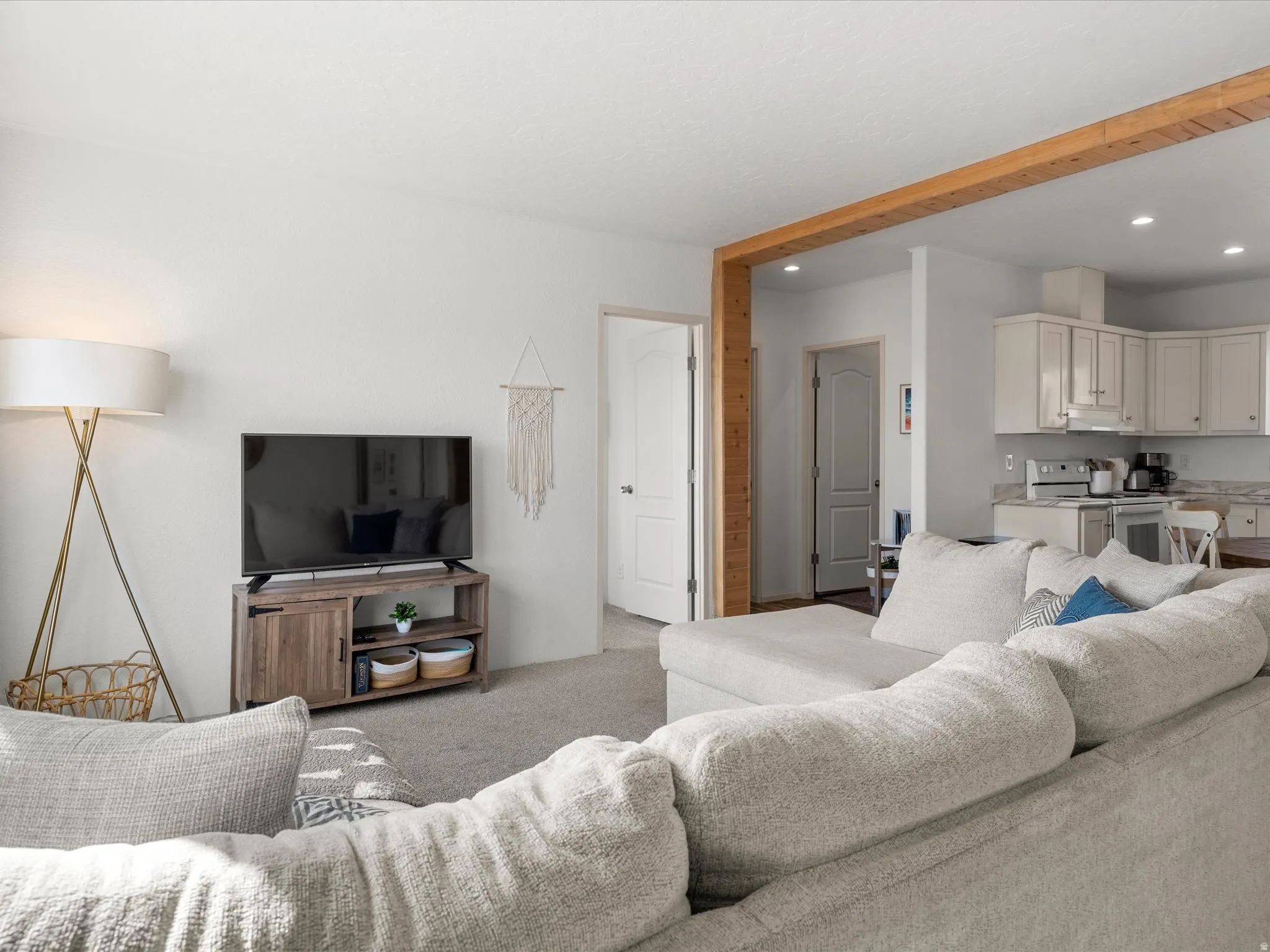 Open-concept living area featuring a wood-finish beam, recessed lighting, and soft carpet flooring