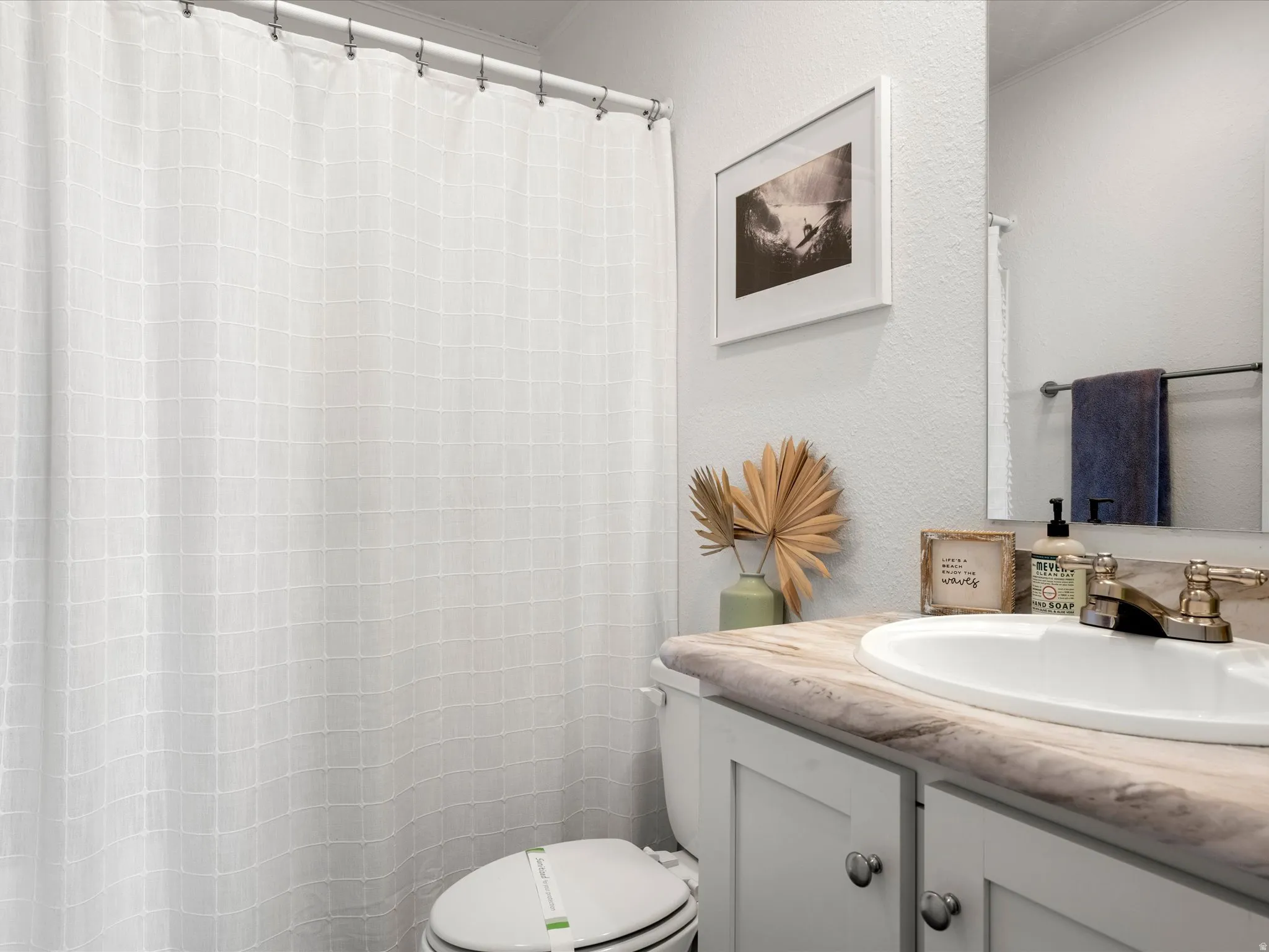 Bathroom featuring a white paneled vanity with chrome hardware, an integrated sink, a vanity mirror, and a full shower with a white curtain