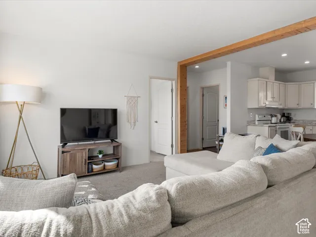 Open-concept living area featuring a wood-finish beam, recessed lighting, and soft carpet flooring