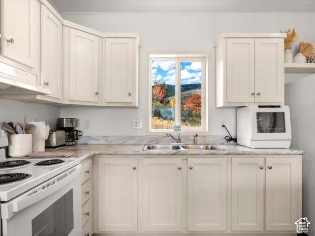 White cabinetry, neutral countertops, stainless steel double basin sink, electric range, and a window with a natural backdrop