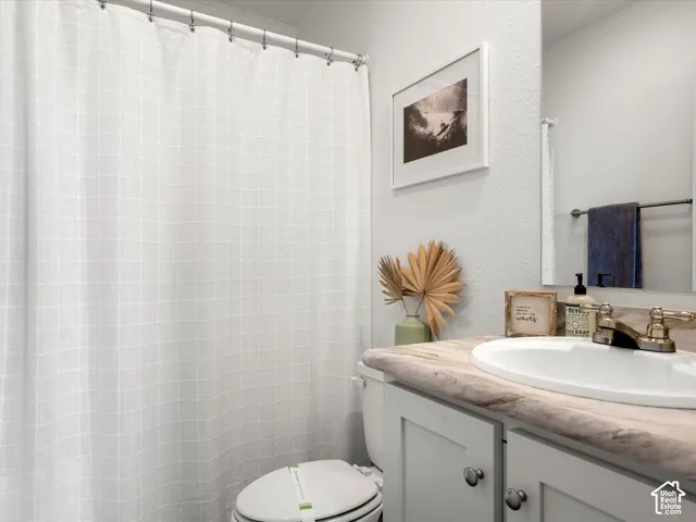 Bathroom featuring a white paneled vanity with chrome hardware, an integrated sink, a vanity mirror, and a full shower with a white curtain