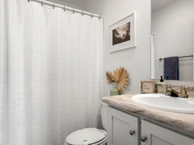 Bathroom featuring a white paneled vanity with chrome hardware, an integrated sink, a vanity mirror, and a full shower with a white curtain