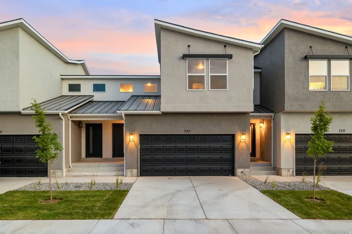 Modern townhome exterior featuring an asymmetrical roofline, stucco siding, and a black paneled garage door